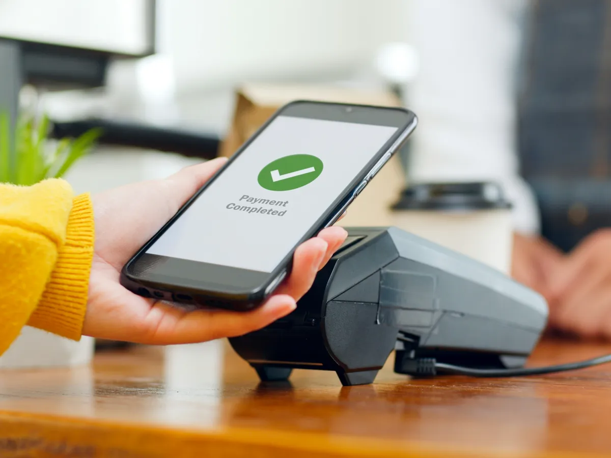 A phone showing a completed payment held over a card terminal