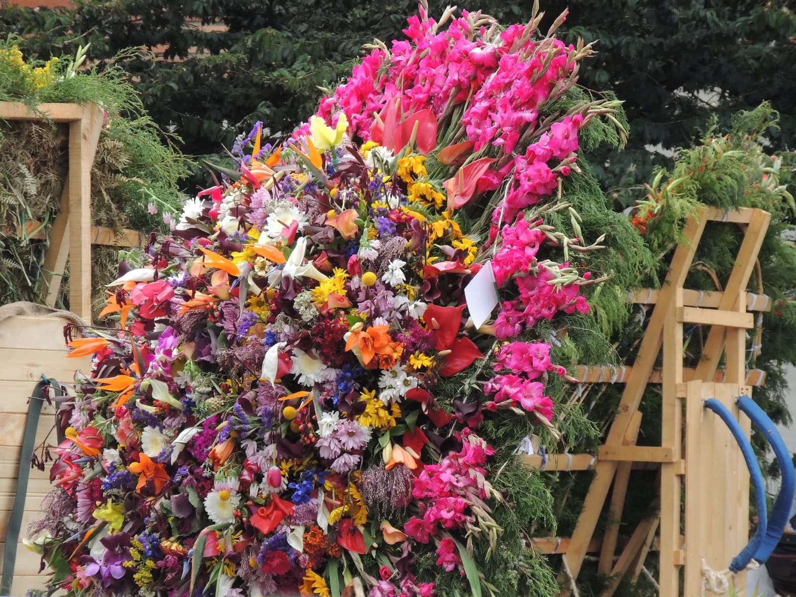 A silleta packed with pink, orange and yellow flowers on a wooden frame