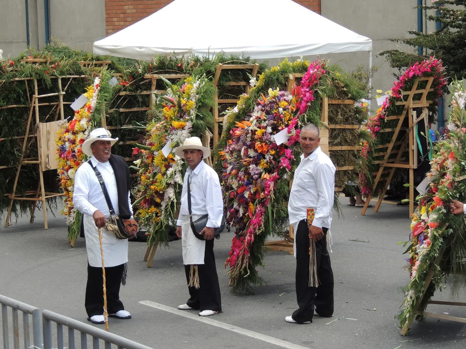 Silleteros in white shirts and straw hats carrying flower displays on their backs at the Desfile de Silleteros
