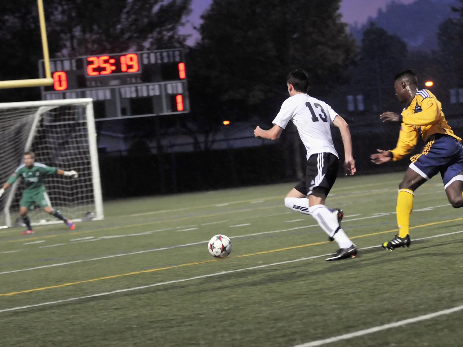 University men’s soccer players racing for the ball under the lights