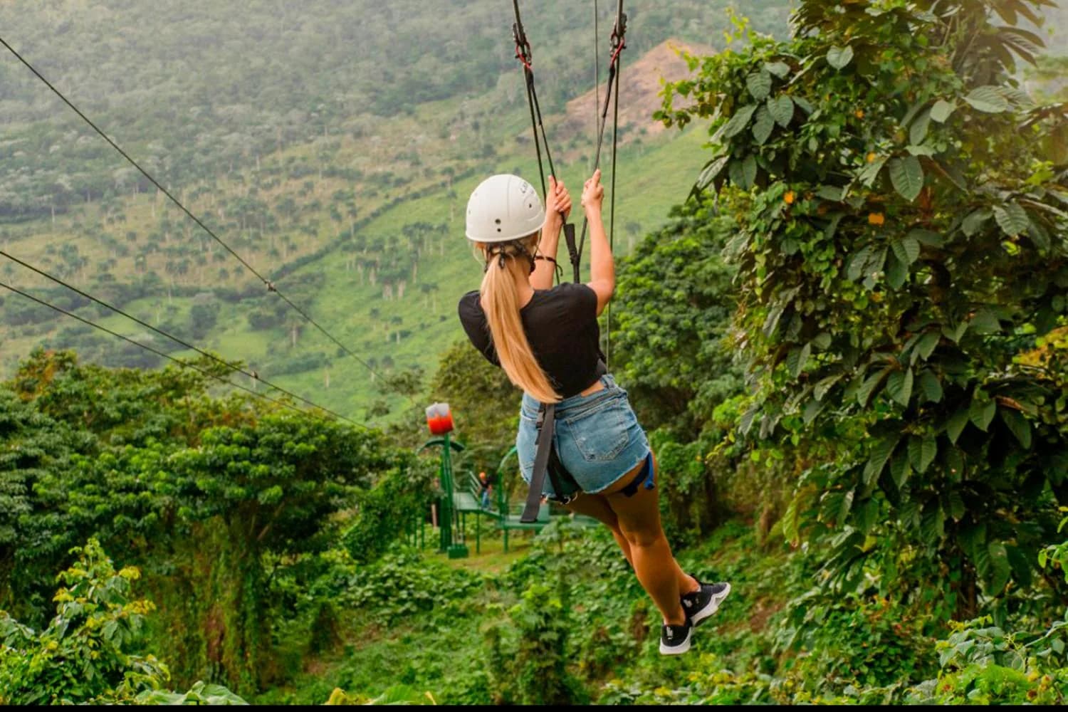 A zipline rider crossing high above a green valley
