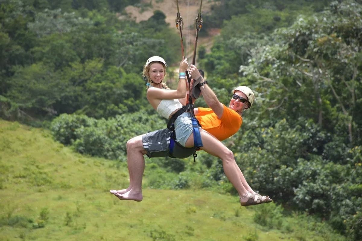 Two riders crossing a treetop zipline side by side