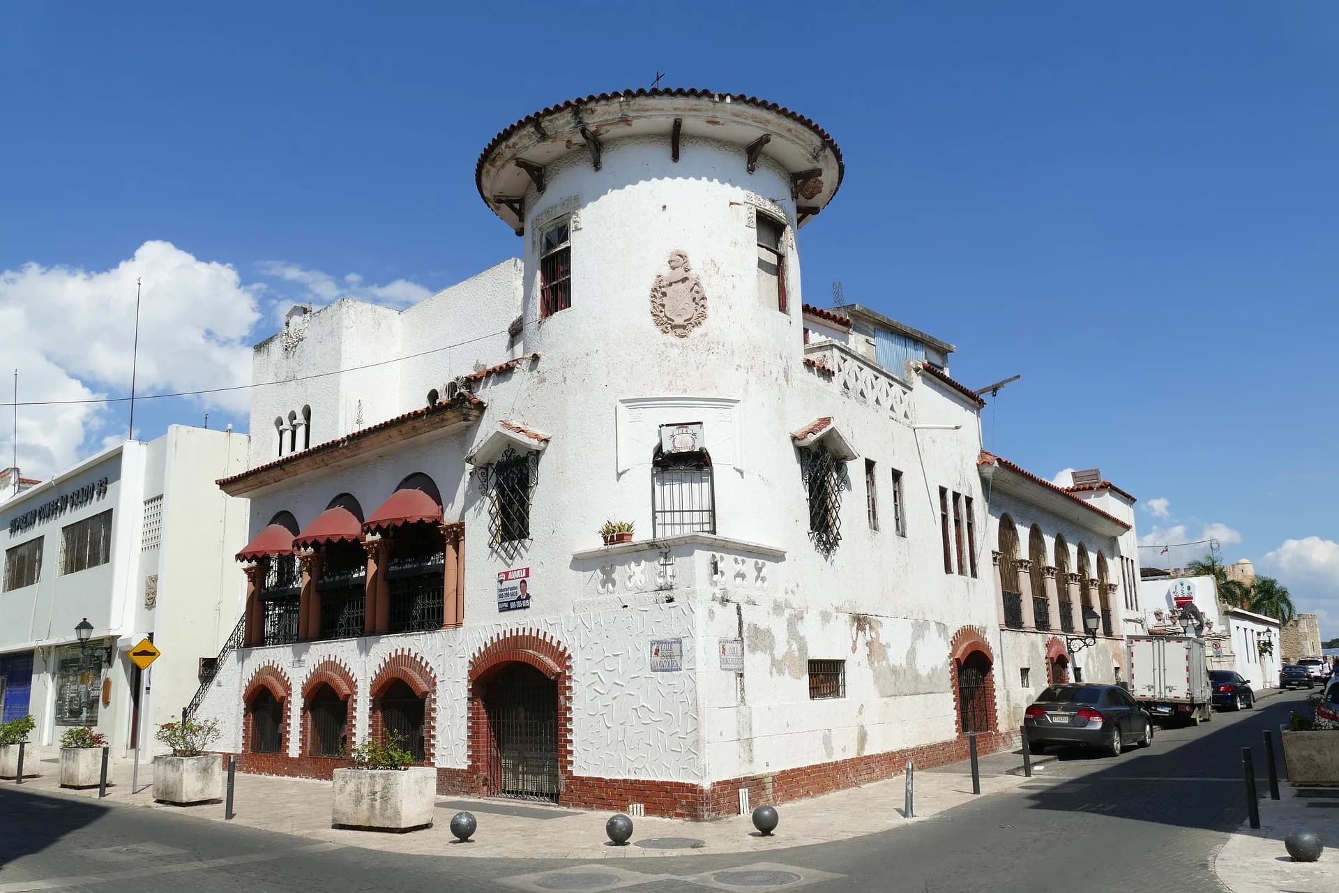 A white colonial corner building with a round tower on a sunny street