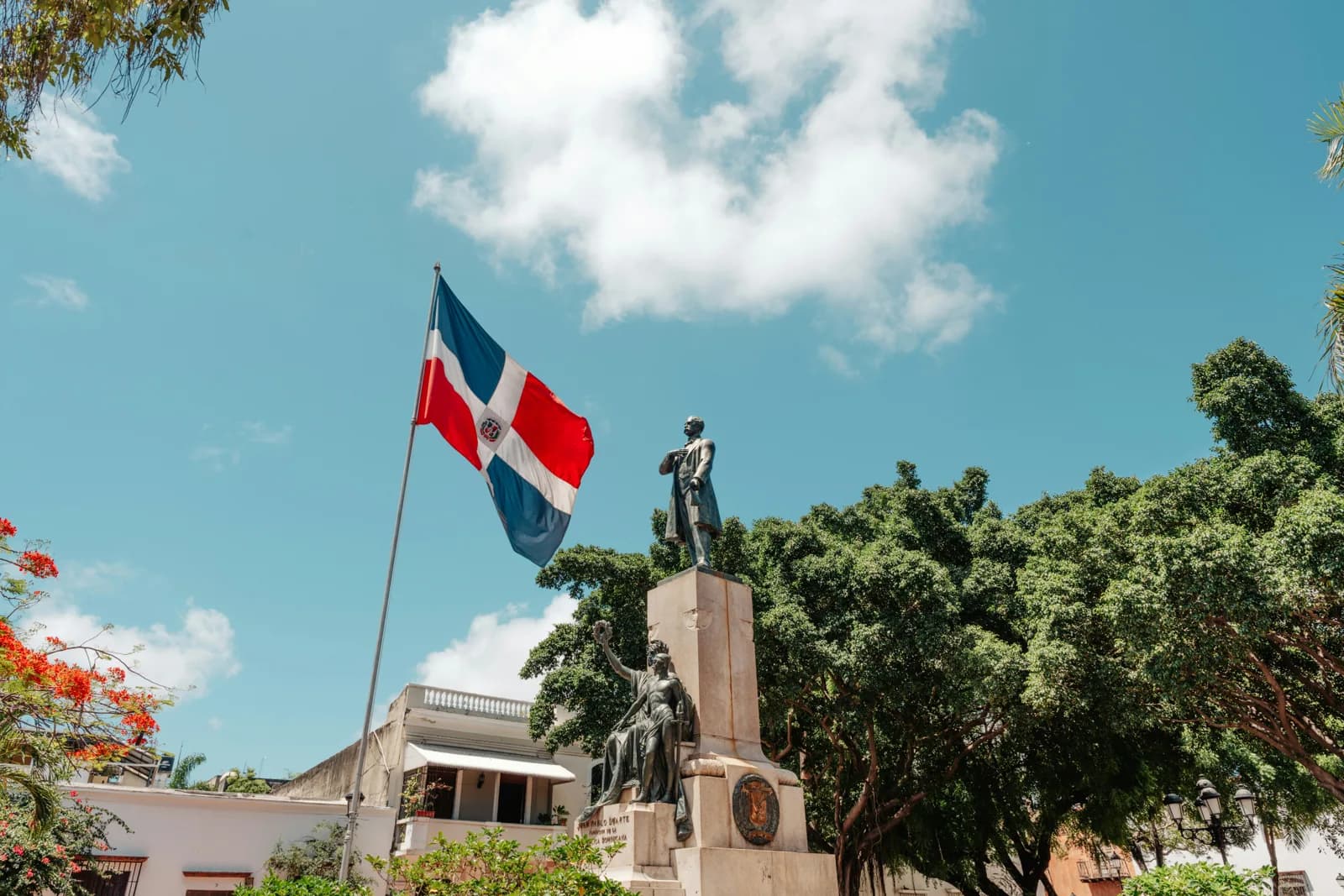The Dominican flag flying above a monument in a leafy square