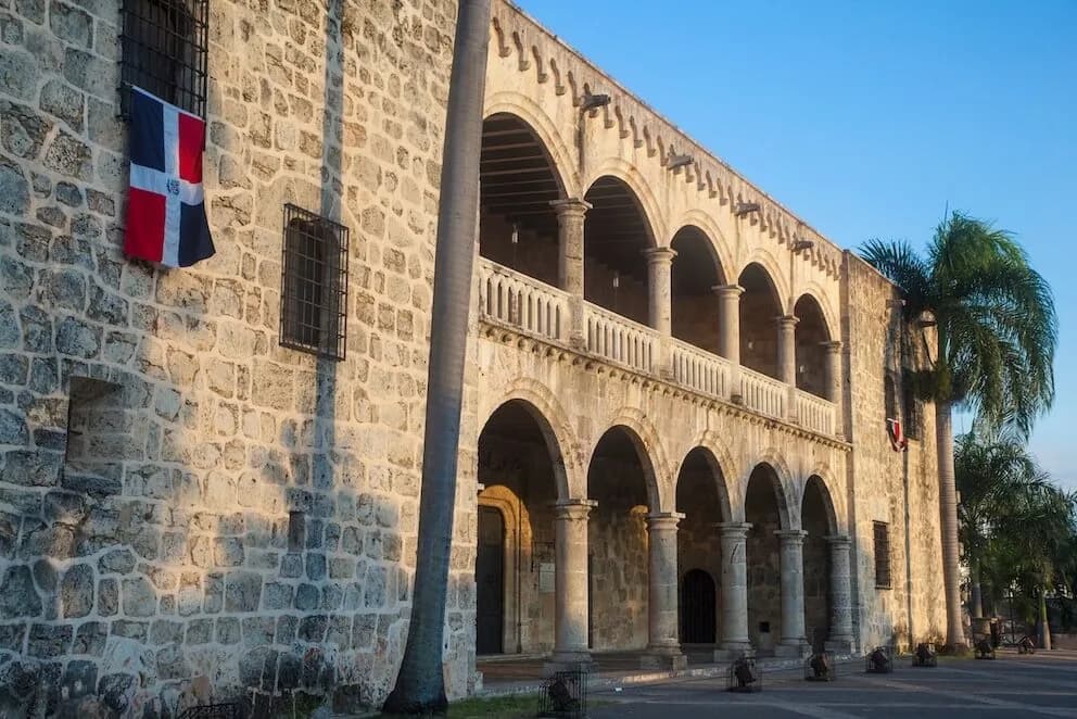 The Dominican flag flying in front of a colonial stone palace
