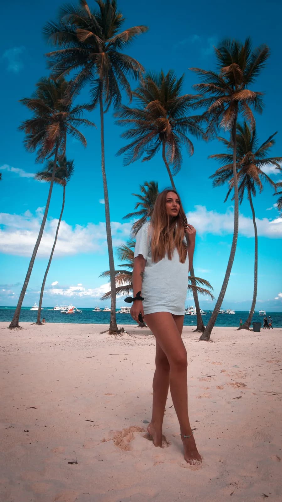 A visitor walking on a sandy beach beneath tall palms