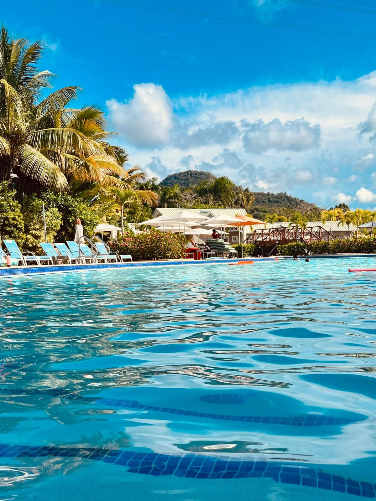 Blue swimming-pool water with loungers and tropical hills beyond