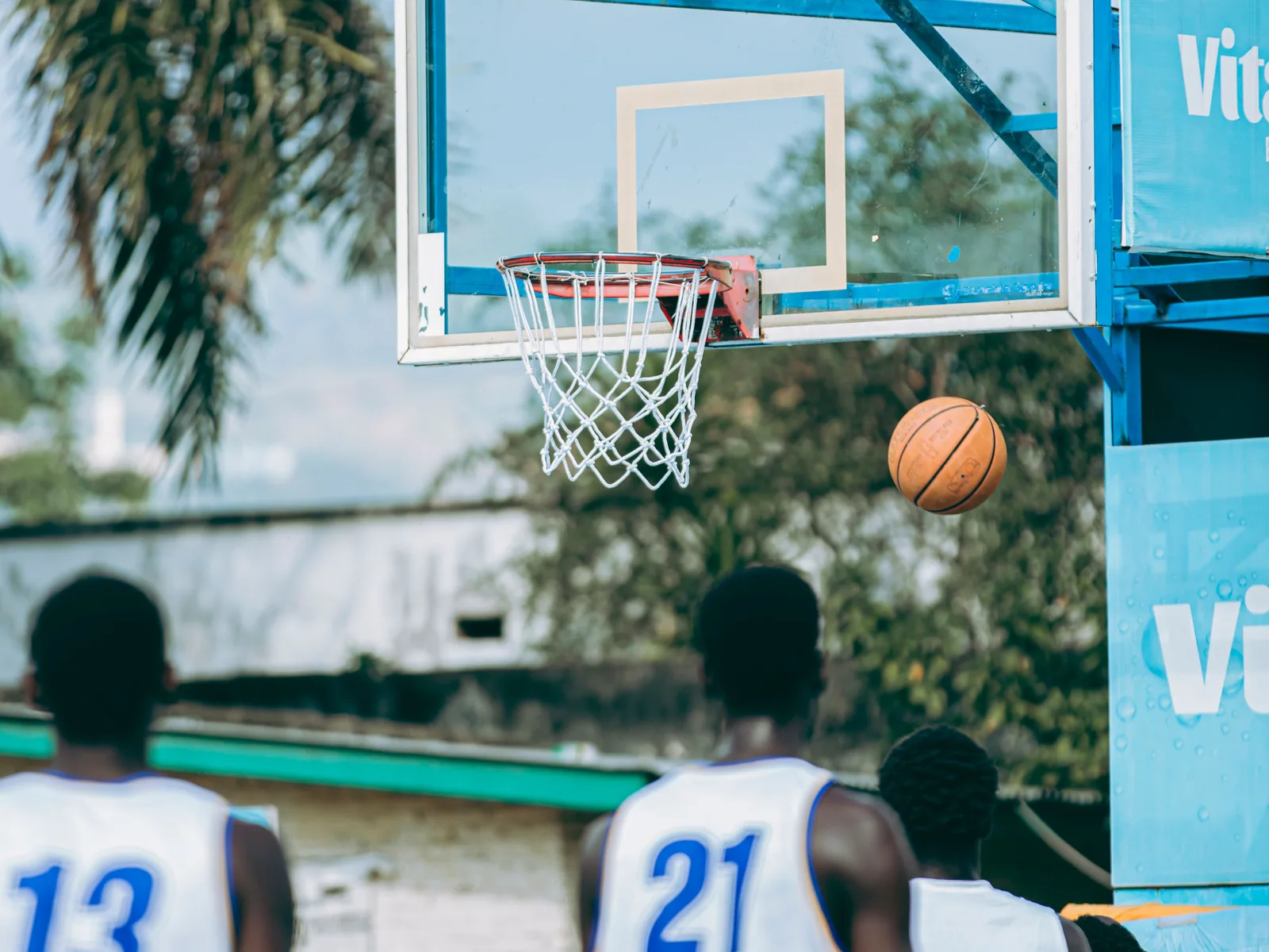 A basketball dropping through the hoop on an outdoor Dominican court as players look on