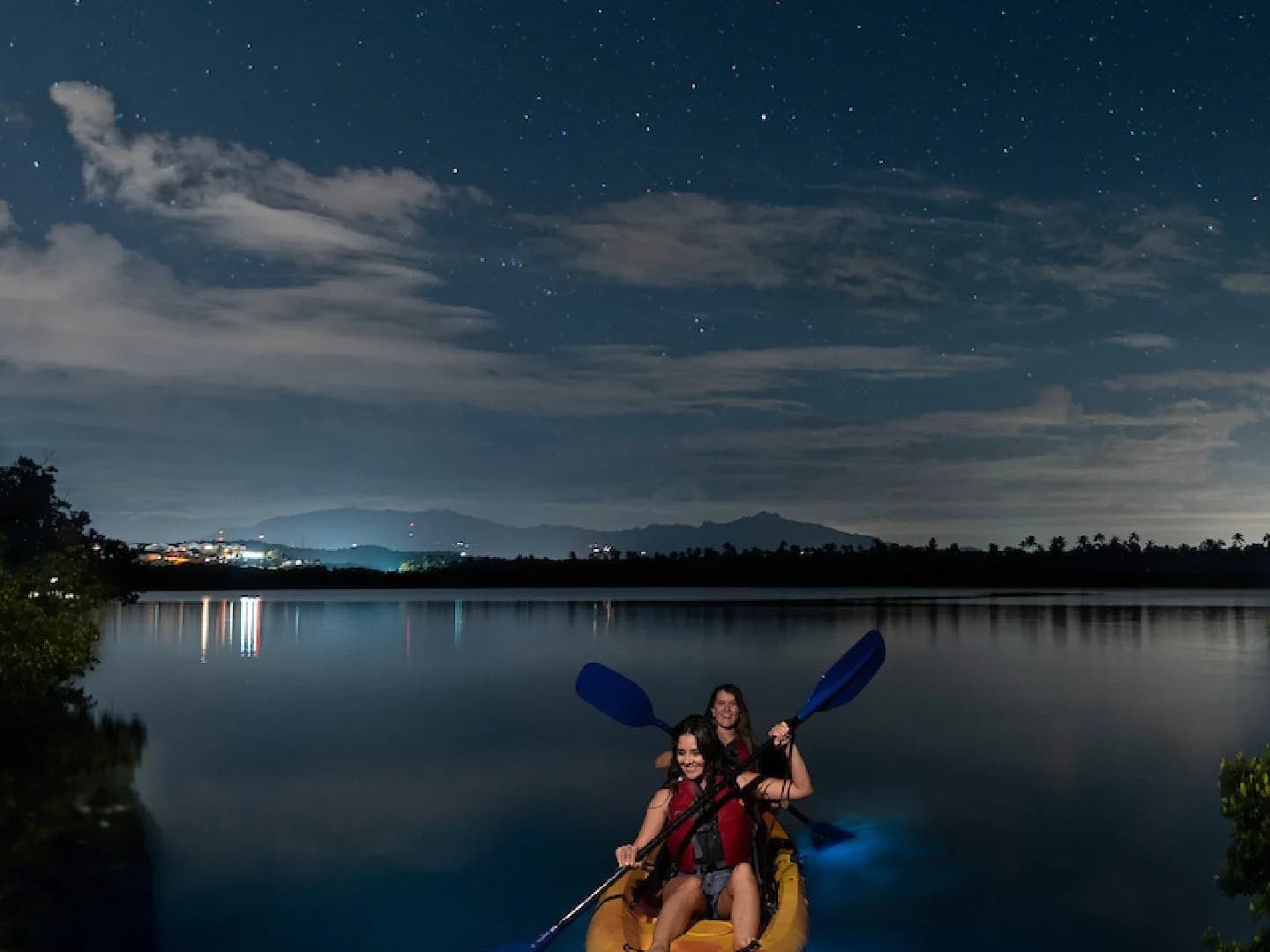 Two people paddling a kayak on a bioluminescent bay under a starry sky