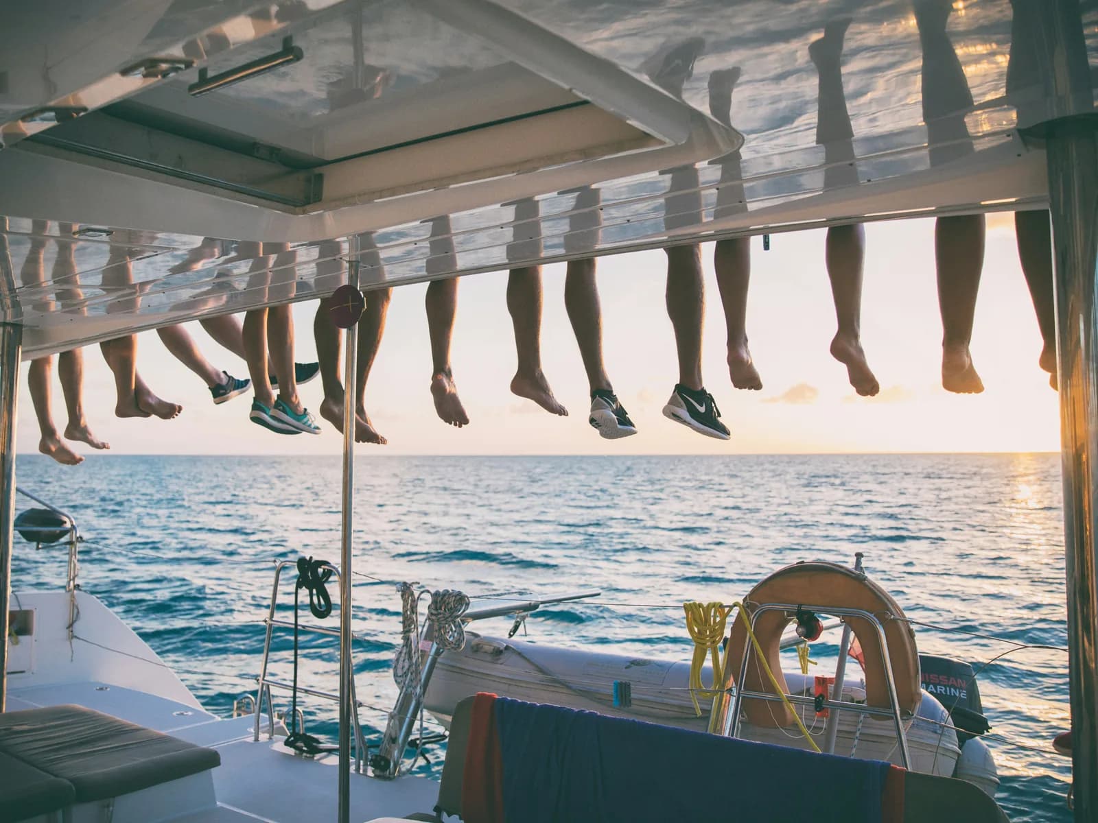 Feet dangling from the deck of a catamaran over the sea at sunset