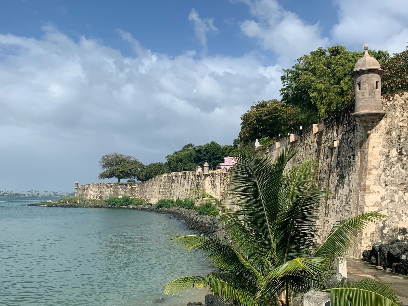 The old city walls of San Juan with a sentry box and palms along the shore