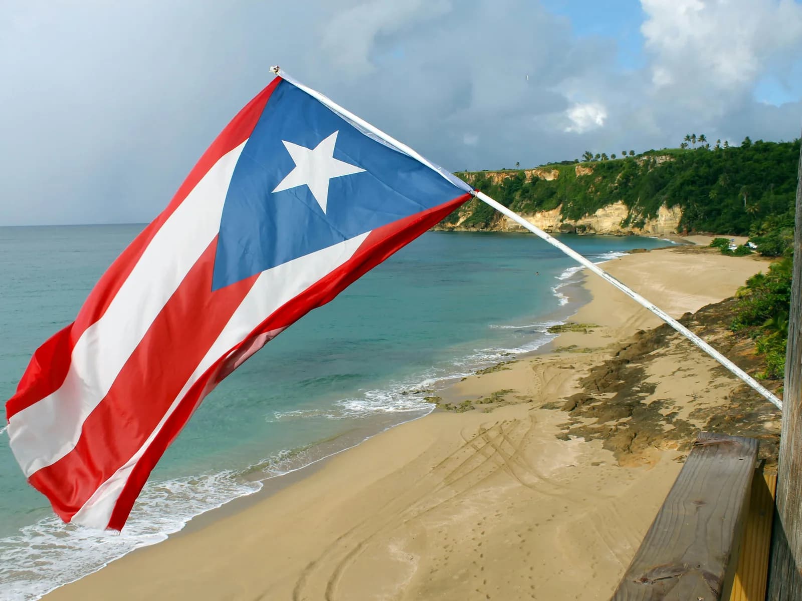 The flag of Puerto Rico flying above a beach and headland