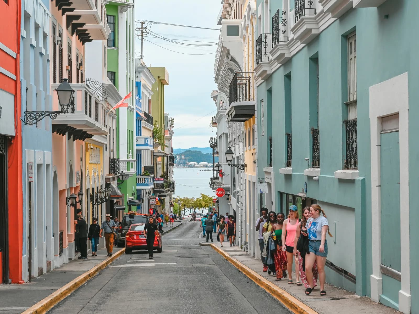 People walking a colourful street in Old San Juan with the sea at the end of it