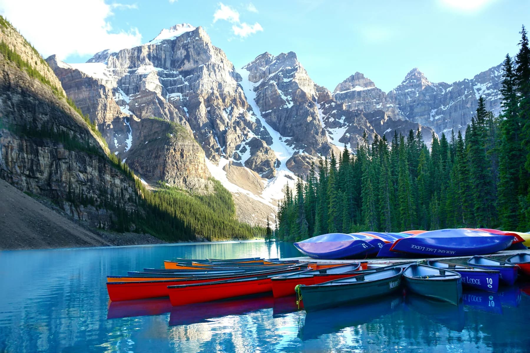 Bright canoes beside a turquoise lake surrounded by mountain peaks